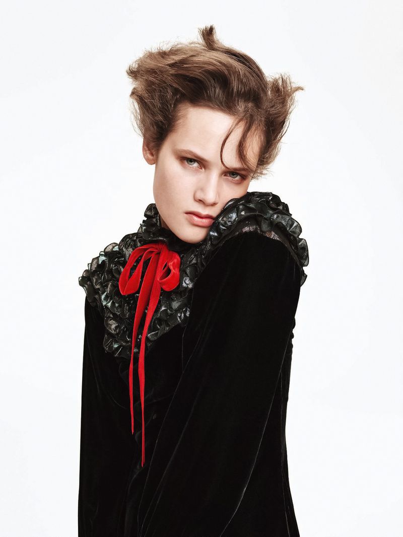 Portrait of an adult female with styled brown hair, wearing a black velvet dress with a red bow against a plain white background.