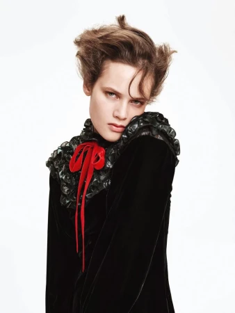 Portrait of an adult female with styled brown hair, wearing a black velvet dress with a red bow against a plain white background.