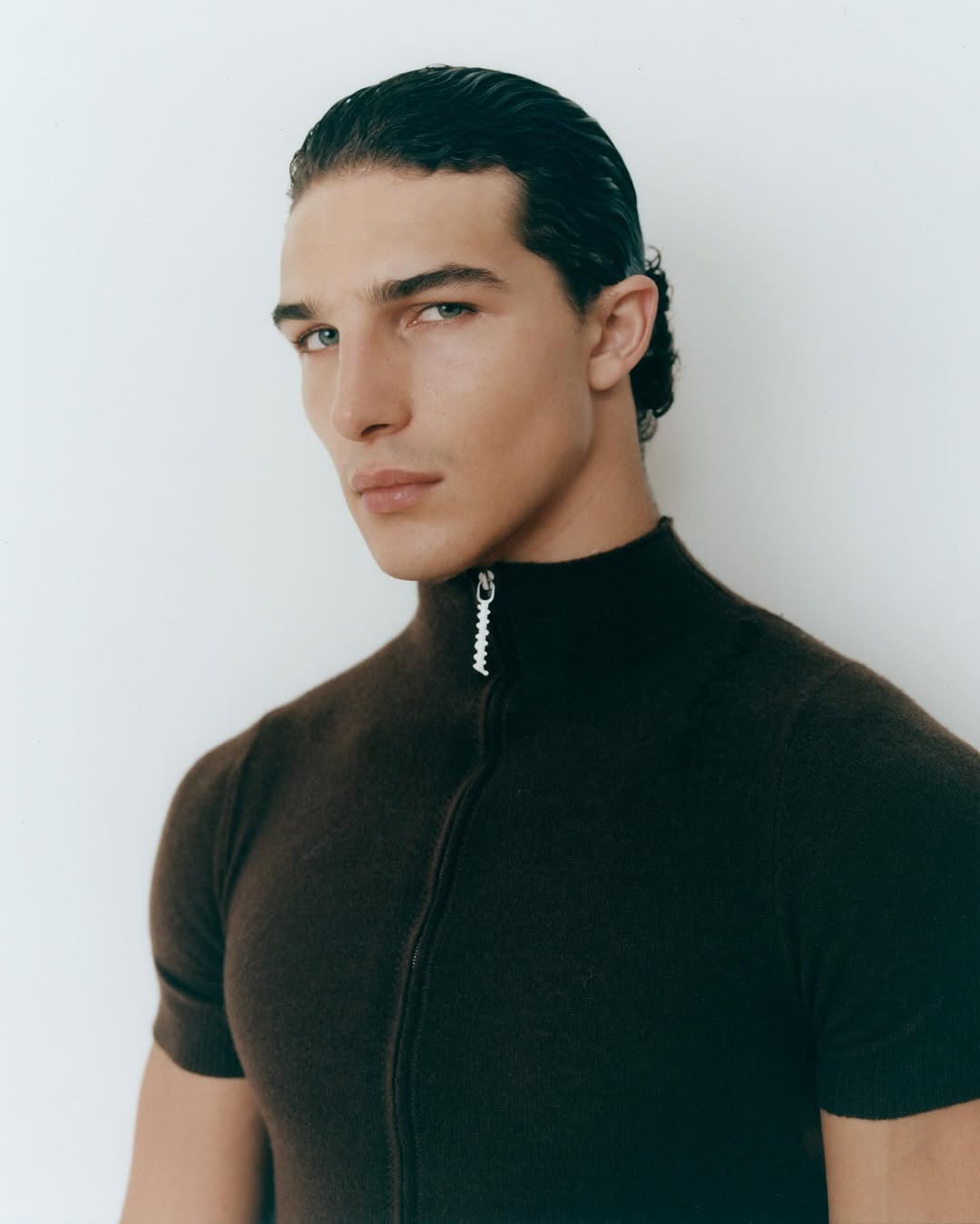 Portrait of a man wearing a dark brown zip-up mock neck top against a plain white background
