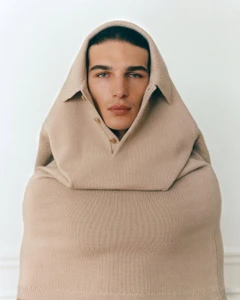 Man wearing a beige knitted polo shirt pulled up over his head like a hood against a plain white background