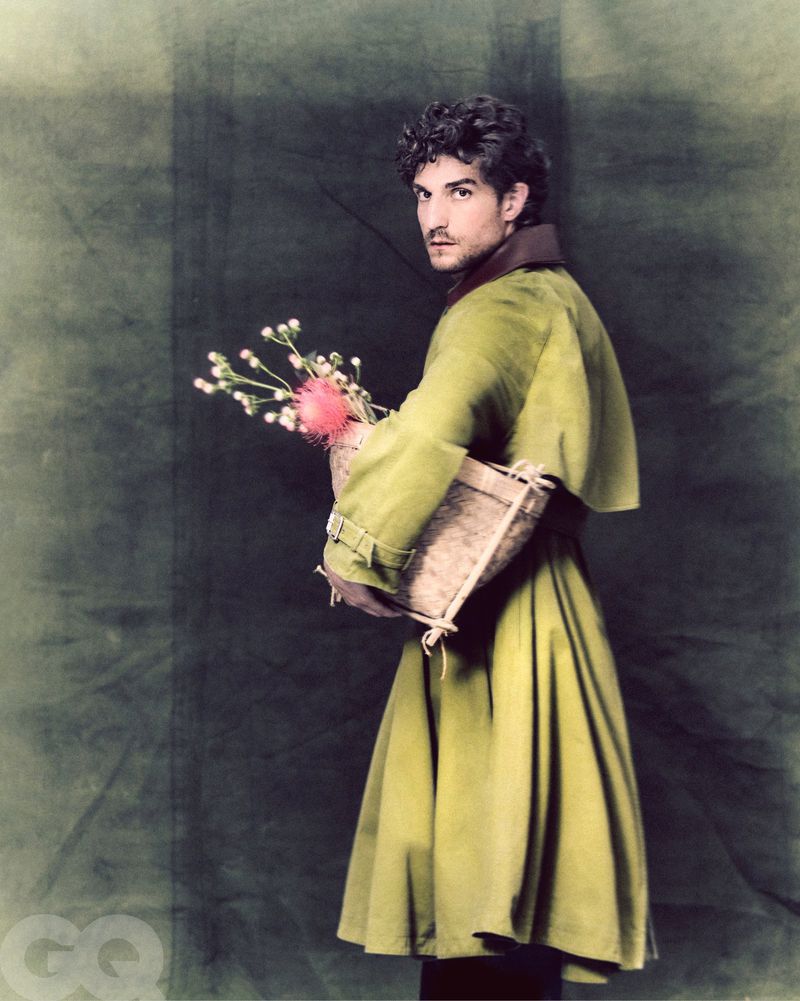 Man in a green coat holding flowers in a basket on green background. Portrait shot of a man in fashionable outerwear.