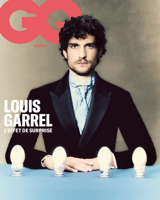 Magazine cover featuring Louis Garrel wearing a suit jacket and bow tie seated at a table with eggs on pedestals and the GQ logo.