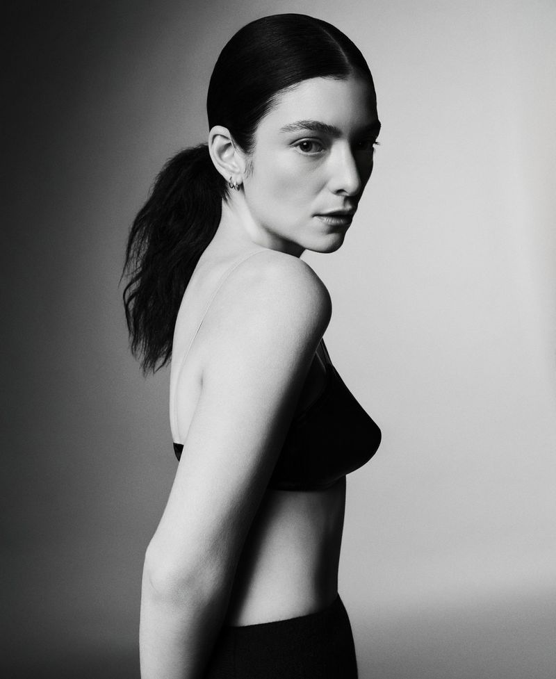 Monochrome portrait of a woman with dark hair in a ponytail wearing a black bra top, captured in a studio with soft, diffused lighting.