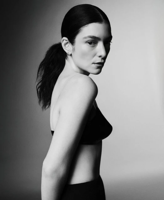 Monochrome portrait of a woman with dark hair in a ponytail wearing a black bra top, captured in a studio with soft, diffused lighting.