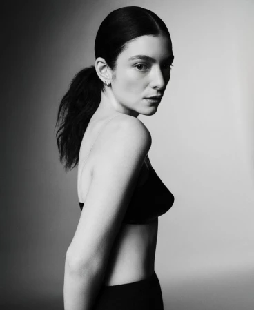Monochrome portrait of a woman with dark hair in a ponytail wearing a black bra top, captured in a studio with soft, diffused lighting.