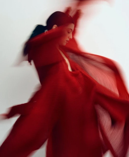 Woman in motion wearing red dress against white background, blurred motion effect, artistic fashion photography, studio lighting, fashion editorial.