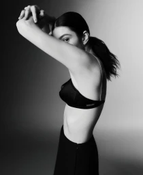 Black and white portrait of singer Lorde in profile wearing a black bra top and skirt with arms raised across her face.