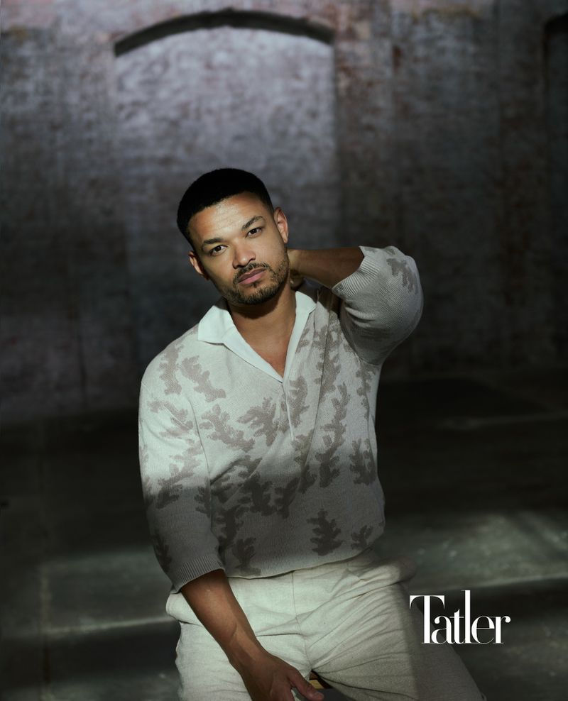 Portrait of a man in a patterned shirt standing in front of an old brick archway inside a building with shadows and natural light.