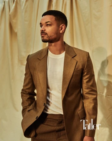 Steven Bartlett posing in a camel brown blazer and white t-shirt against a draped beige fabric backdrop for Tatler.