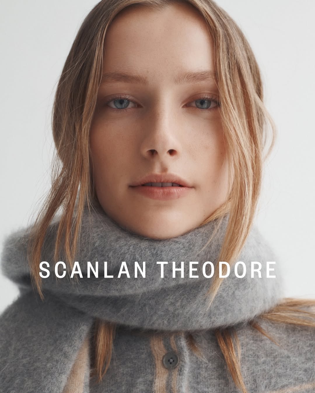 Close-up shot of a young woman with light brown hair wearing a grey scarf and top against a white backdrop. Beauty and fashion.