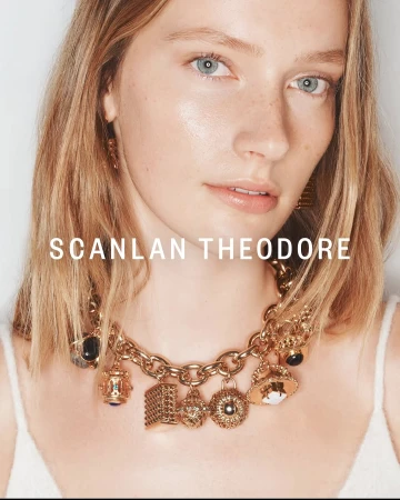 Close-up of a blonde woman wearing a gold chain necklace with several charms. Beauty shot with soft light and a white background.