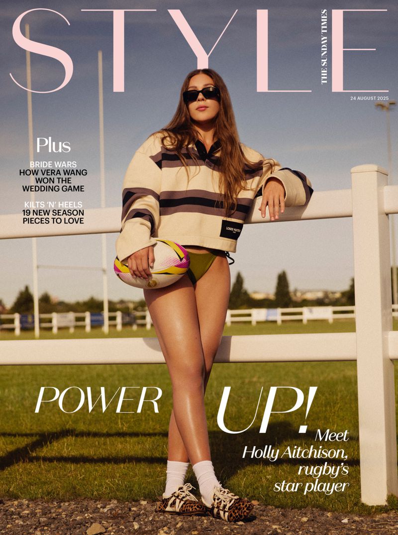 Magazine cover featuring a woman in athletic-inspired fashion holding a rugby ball, photographed outdoors on a grassy field on a sunny day.