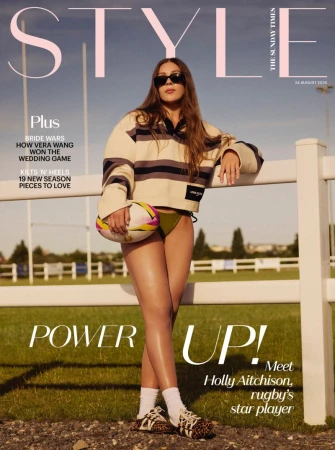 Magazine cover featuring a woman in athletic-inspired fashion holding a rugby ball, photographed outdoors on a grassy field on a sunny day.