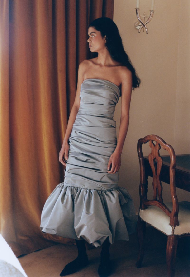 Elegant woman poses in a silver strapless dress with a ruffled hem, complemented by pointed black boots against a neutral backdrop.