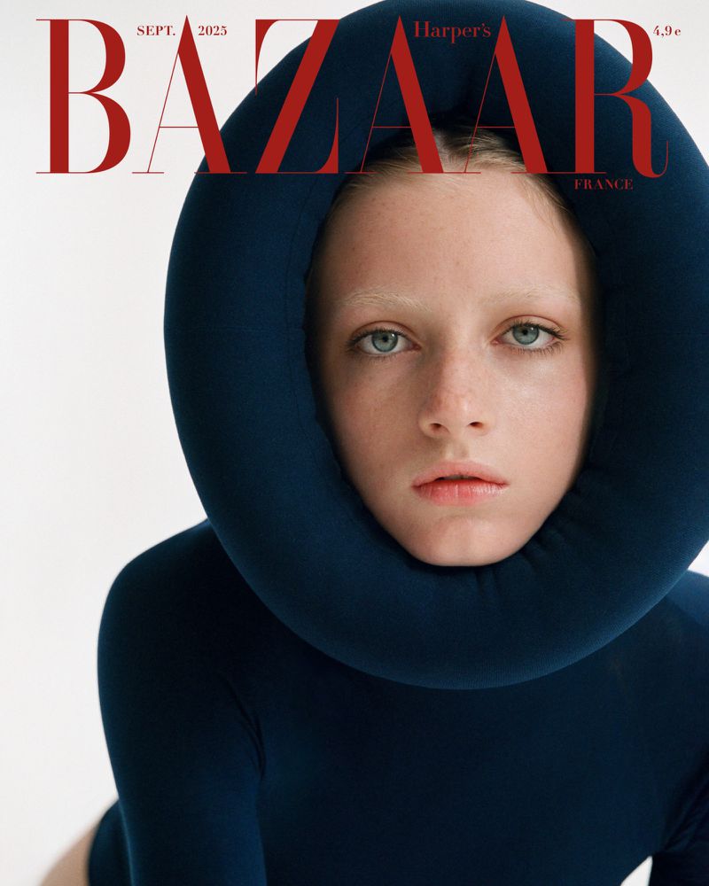 Close-up portrait of a model wearing a dark blue garment with a large padded collar against a white background.