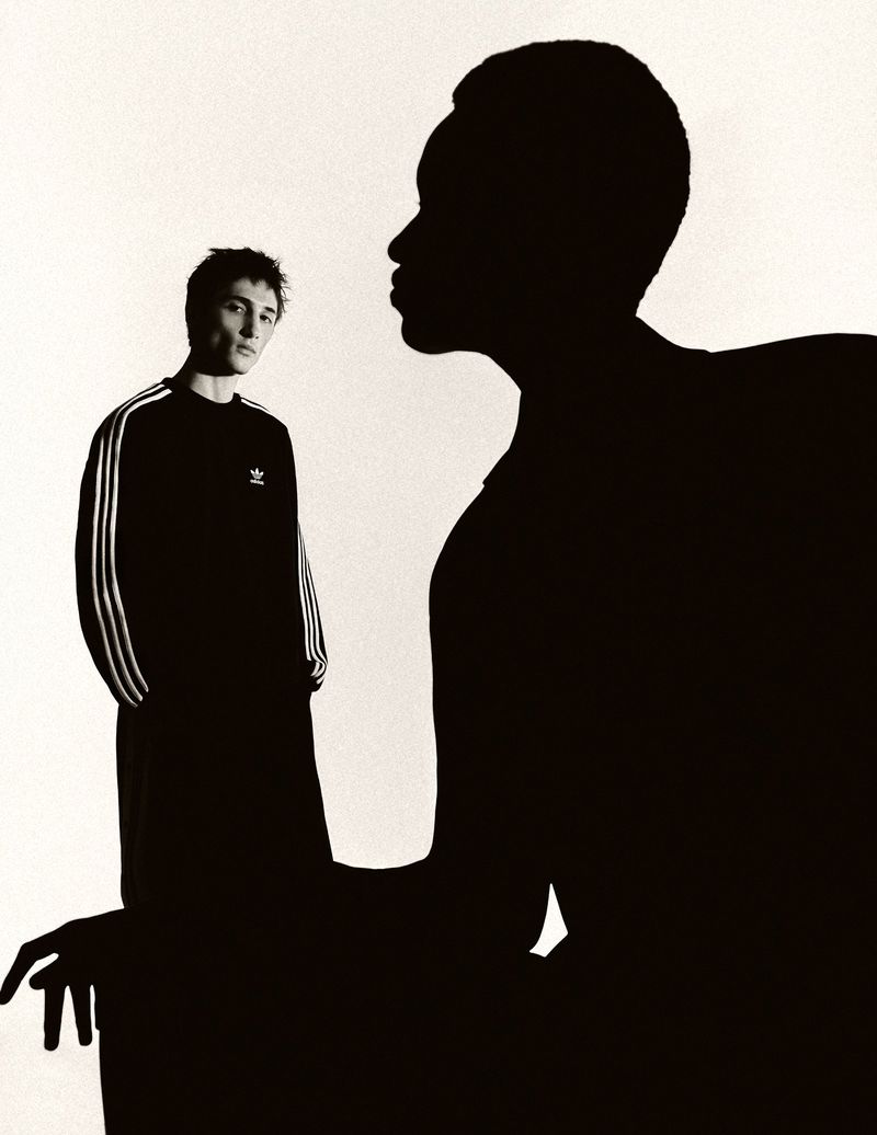 Fashion shot of two adults, one in silhouette, against a white background, wearing branded activewear in a studio setting.