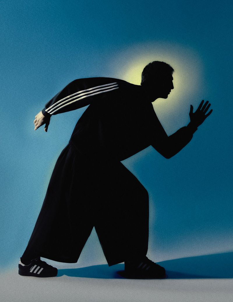Silhouette of a man in sportswear running with outstretched arms against a gradient blue studio backdrop with backlighting.