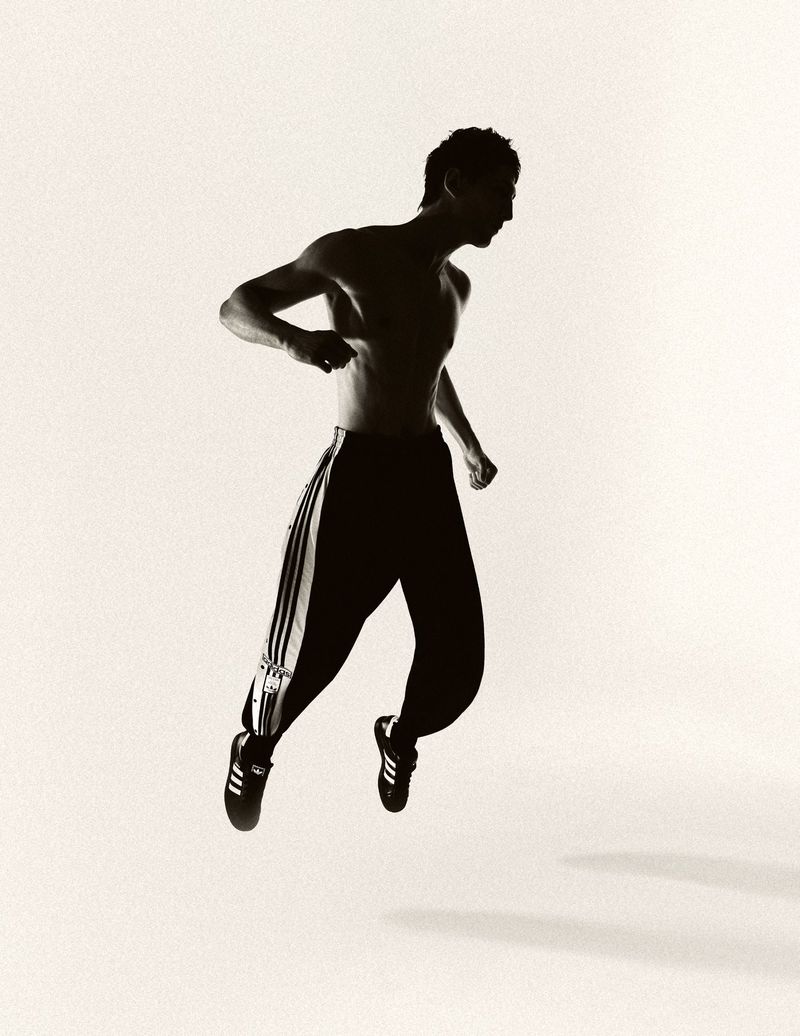 Silhouette of a man in motion jumping in athletic pants and shoes on a white background, showcasing fitness and movement.