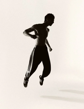 Silhouette of a man in motion jumping in athletic pants and shoes on a white background, showcasing fitness and movement.