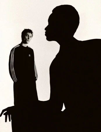 Model wearing a black Adidas three-stripe sweatshirt framed behind a large black silhouette profile against a white background.