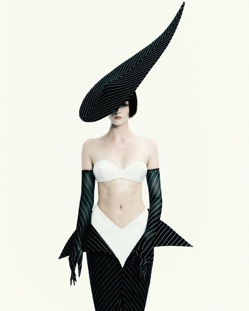 Woman in avant-garde black and white pinstripe hat and dress posing in a studio. High fashion and studio lighting create a striking visual.