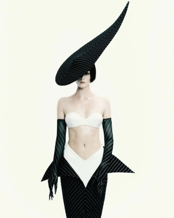 Aylah Peterson wearing a sculptural pointed pinstripe hat, matching gloves, and white bandeau top against a white backdrop.