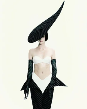 Aylah Peterson wearing a sculptural pointed pinstripe hat, matching gloves, and white bandeau top against a white backdrop.