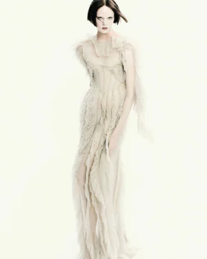 Model wearing a textured cream ruffled gown against a plain white studio background in a fashion portrait.