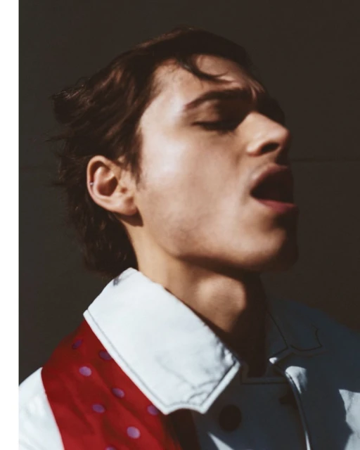 Portrait of a light-skinned young adult male with dark hair in an open-mouth pose, wearing a white shirt and a polka-dot scarf.