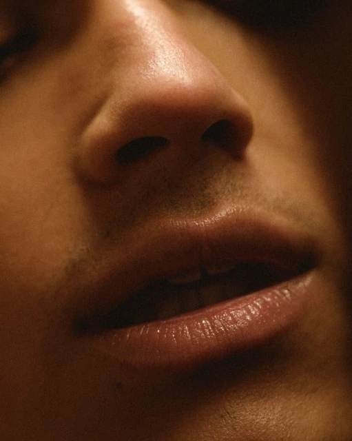 Close-up portrait of an adult male's face showing his nose and lips in warm, low-key lighting creating a sensual, intimate mood.