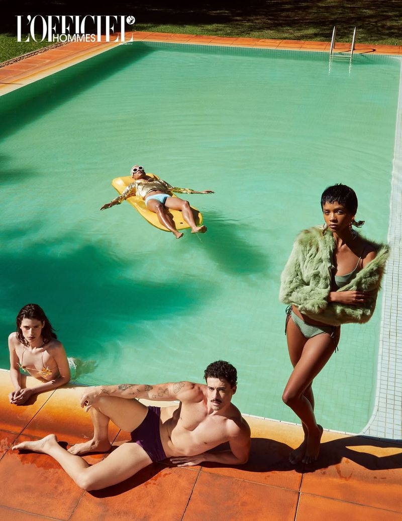 Swimsuit fashion editorial shot featuring diverse group of models posing near a pool in swimsuits and stylish accessories on a sunny day.