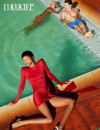 Editorial fashion shot of a woman in a red dress beside a pool, with two men in swimwear in the background; shot with bright, summery lighting.