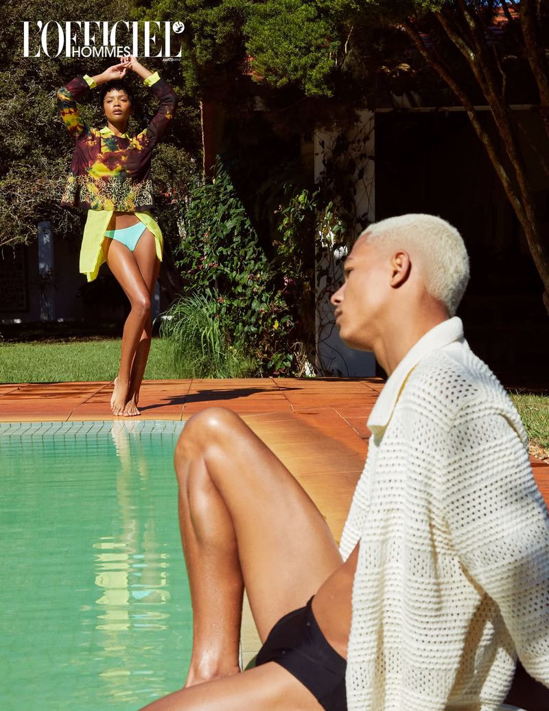 Two fashion models pose outdoors near a pool; one model stands and wears a yellow skirt and patterned top; the other sits in a knitted shirt.