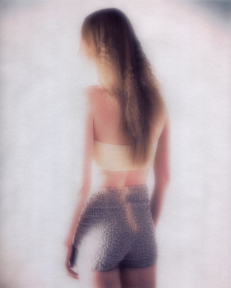 Back view of a woman in a crop top and shimmering shorts against a blurred backdrop, highlighting fashion and style.