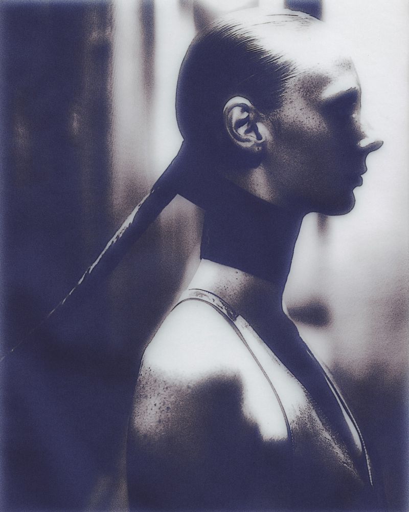 Portrait of a woman in profile with sleeked-back hair, showcasing a minimalist aesthetic and cool-toned monochrome color palette.