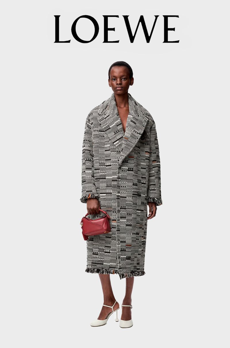 Model wearing a patterned tweed coat, holding a red handbag, in white slingback heels against a light grey studio background.