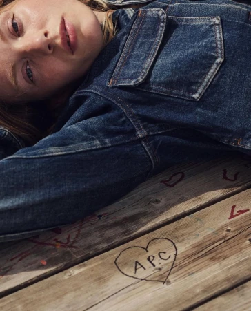 Close-up of a blonde woman in a denim jacket lying on a wooden surface with heart graffiti, showcasing a blend of fashion and art.