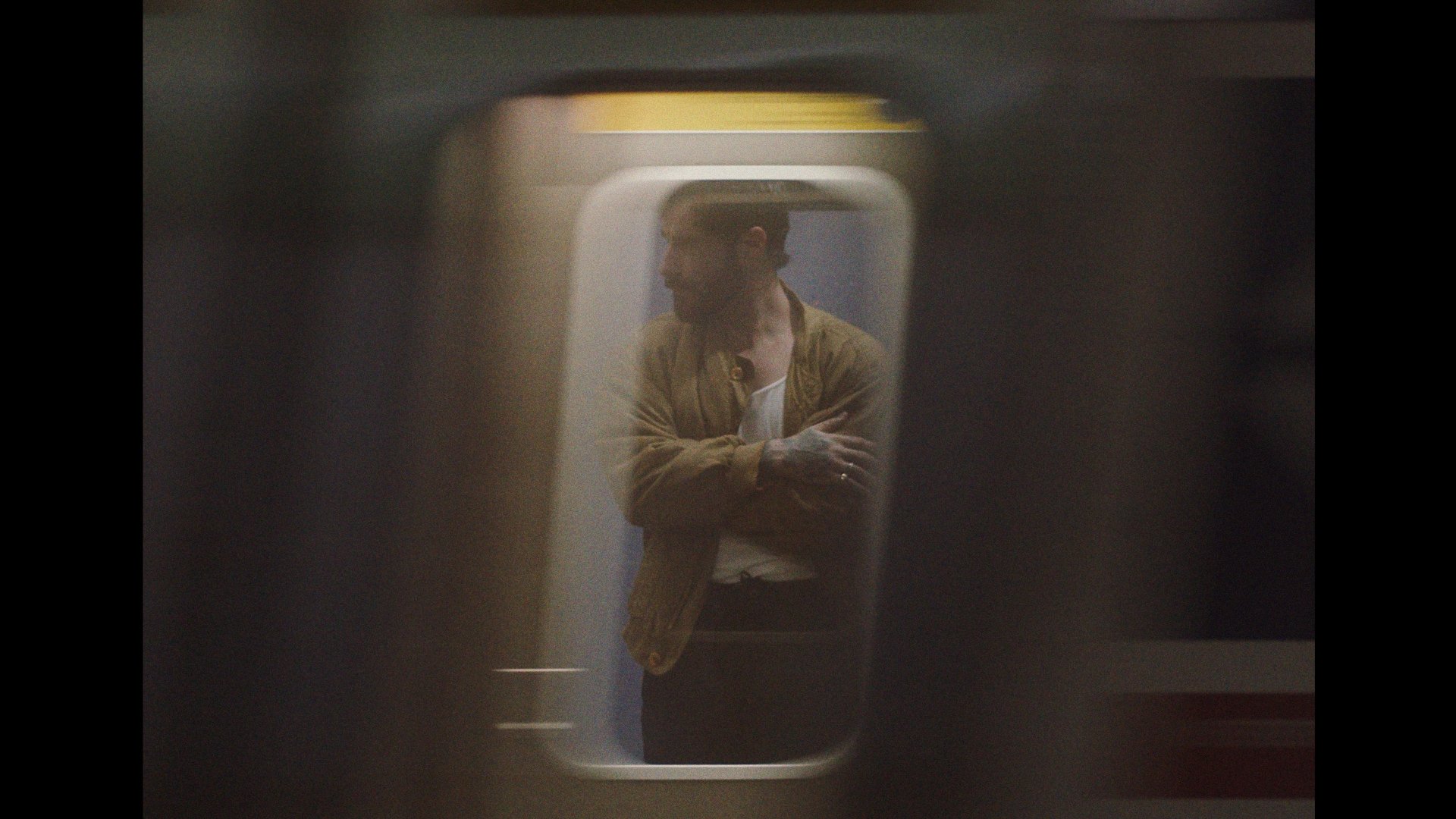 Man with beard and tattoos gazes out of a train window in warm lighting with motion blur, creating a vintage-style visual.