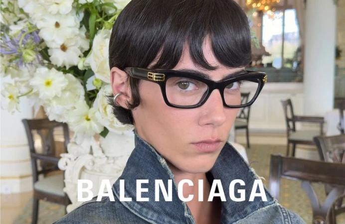 Headshot of an adult woman with short hair and eyeglasses, wearing a blue denim jacket, posing in a dining room with white flowers.