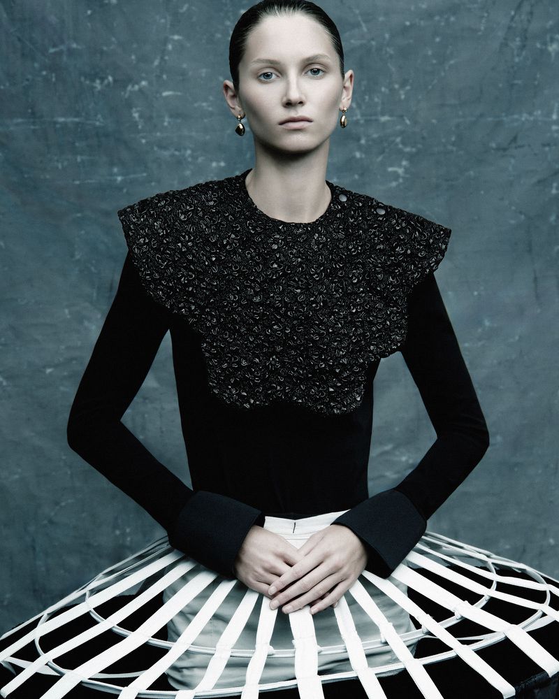 Fashion photography: A woman with slicked-back hair poses in a black top with an embellished collar and a white-striped skirt.