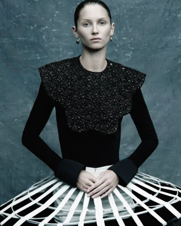 Fashion photography: A woman with slicked-back hair poses in a black top with an embellished collar and a white-striped skirt.
