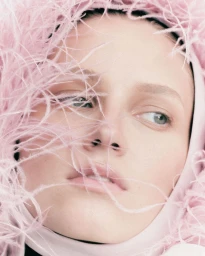 Close-up portrait of a woman framed by wispy pink feathers and light pink hood