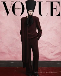 Model wearing a structured burgundy suit and tall black hat against a pink backdrop for Vogue Polska Reconstruction editorial.
