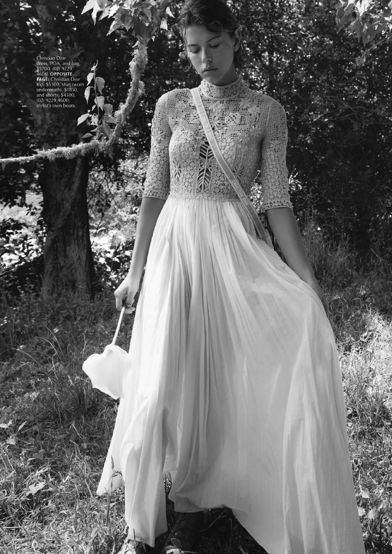 Monochrome image of a woman in a long dress and lace top standing in a wooded area, holding a white parasol. Fashion editorial.