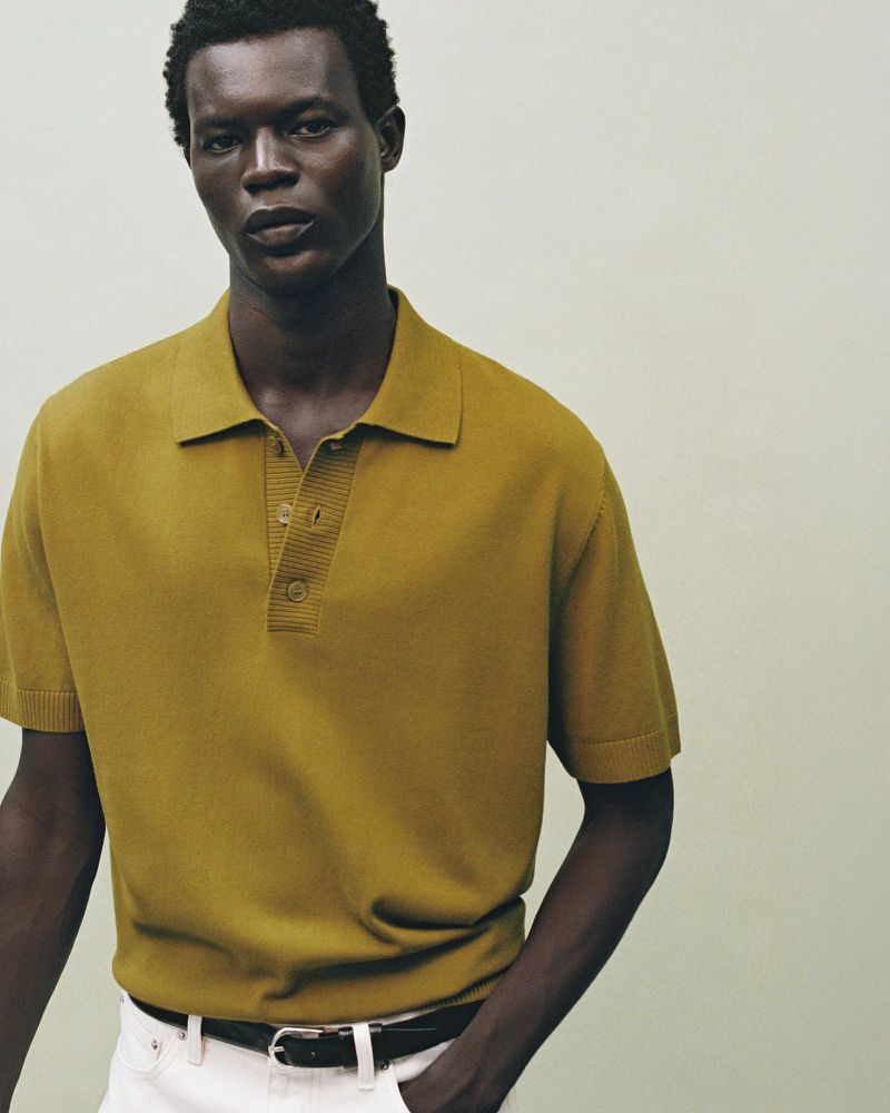 Headshot of an adult male wearing a gold knit polo shirt and white pants against a neutral background in a studio-lit setting.