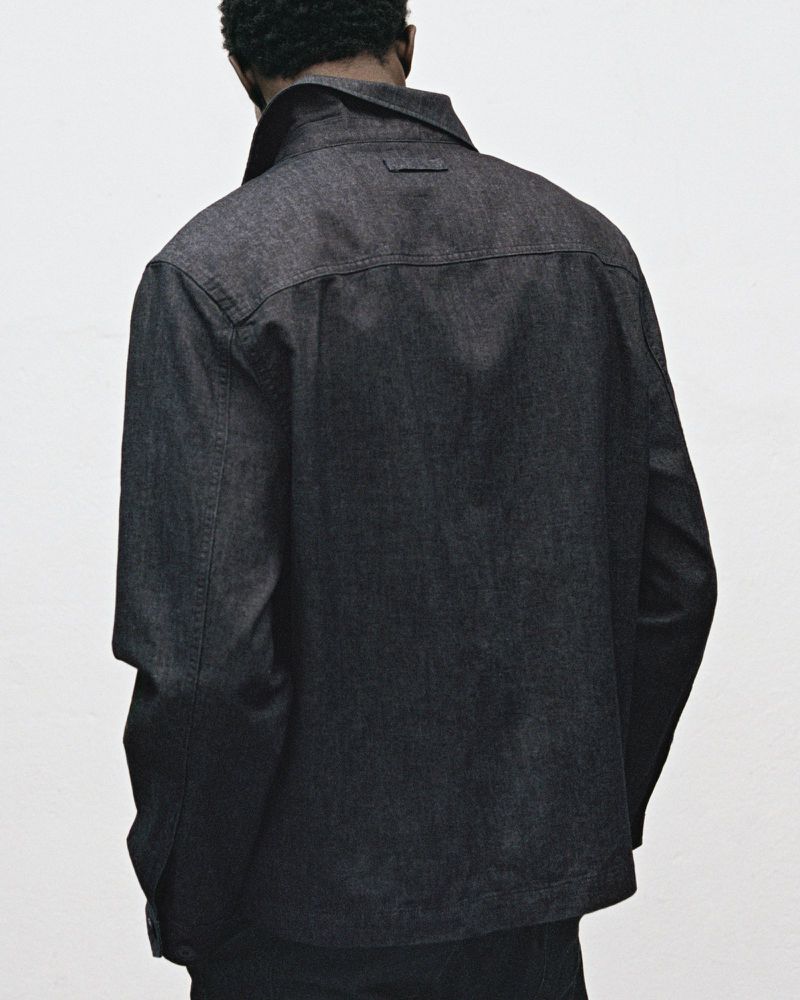 Back view of an adult male wearing a dark denim jacket. The jacket has a classic design with a pointed collar and visible stitching.