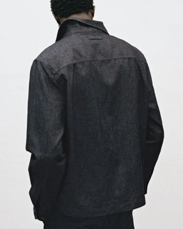 Back view of an adult male wearing a dark denim jacket. The jacket has a classic design with a pointed collar and visible stitching.