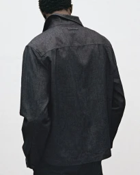 Model seen from behind wearing a dark grey jacket against a neutral white background for Mango editorial