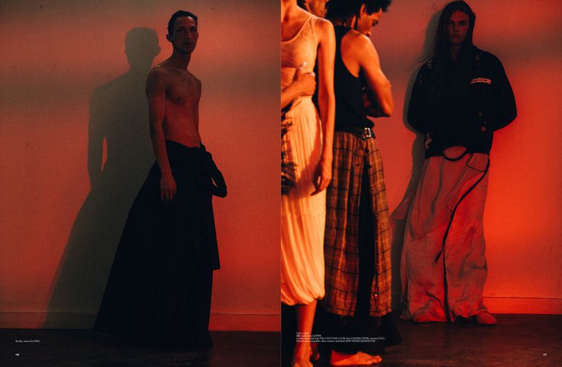 Editorial fashion shot featuring four slender adults in skirts illuminated by a red hue, their expressions neutral against a plain backdrop.