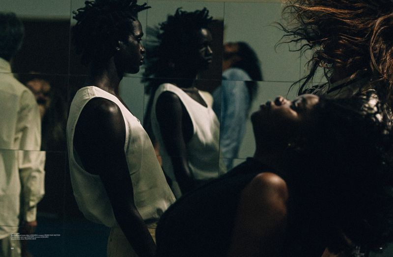 Fashion shot of three dark-skinned women in muted tones against a reflective wall, one with flowing hair, conveying a mood of elegance and artistry.